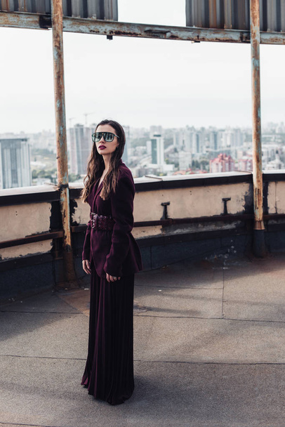 elegante mujer elegante posando en traje de moda de color burdeos y gafas de sol en el techo urbano
  - Foto, Imagen