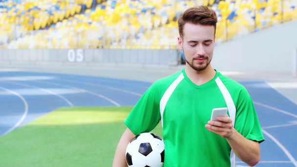 улыбающийся футболист держит мяч и использует смартфон
  - Кадры, видео