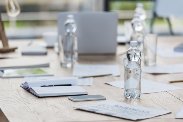selectieve focus van fles met water in de buurt van smartphone, notebook en documenten op houten tafel in vergaderzaal - Foto, afbeelding