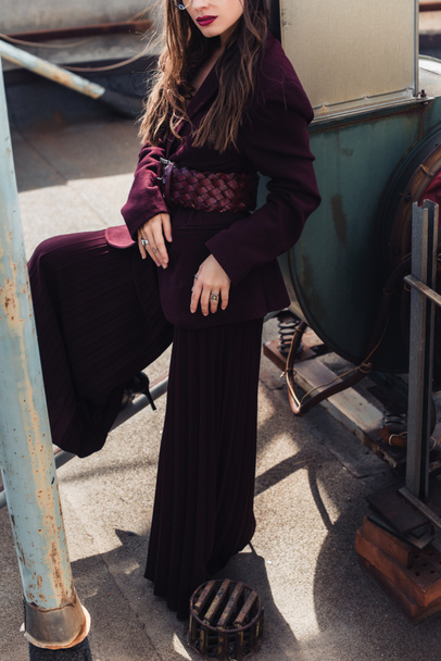 cropped view of stylish girl posing in trendy burgundy suit on urban roof  - Zdjęcie, obraz