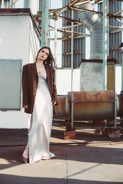 beautiful elegant model posing in silk dress and brown jacket on roof - Foto, Imagem