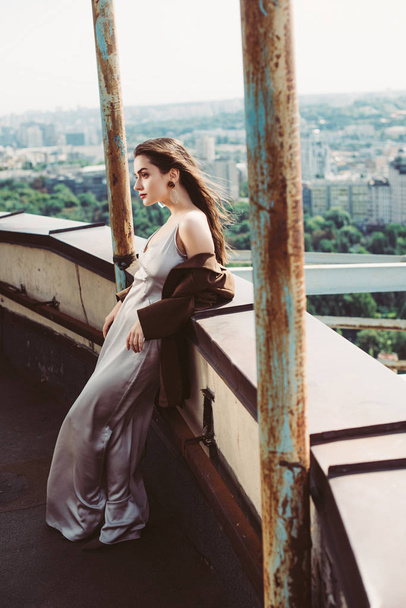 elegante ragazza alla moda posa in abito di seta e giacca marrone sul tetto urbano
 - Foto, immagini