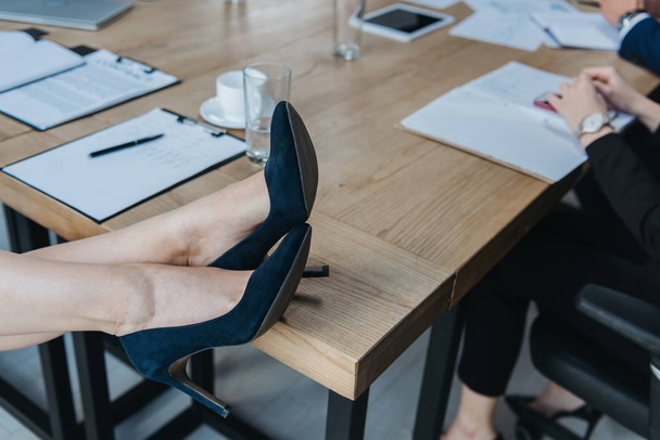 przycięty widok businesswoman w wysokich obcasach buty siedzi z nogami na biurku - Zdjęcie, obraz