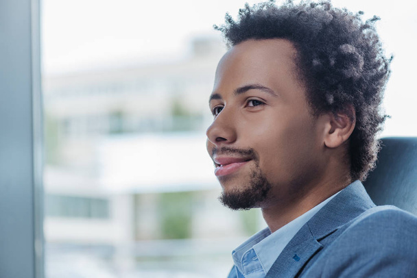 jeune homme d'affaires afro-américain souriant près de la fenêtre dans le bureau
 - Photo, image