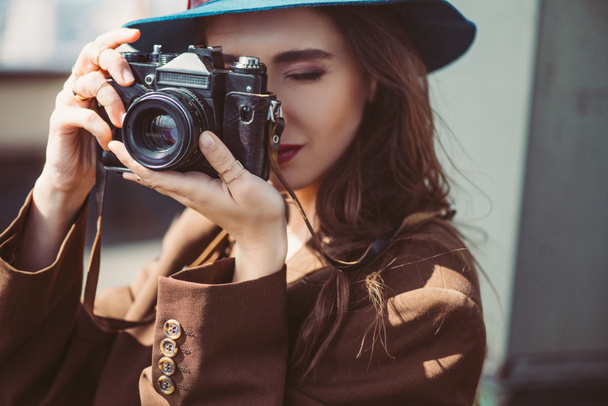 attractive woman in hat taking photos on retro photo camera on roof - Photo, Image