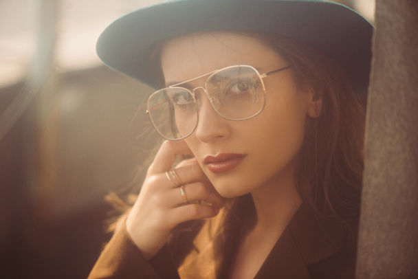 fashionable woman posing in hat, eyeglasses and brown jacket on roof - Photo, Image
