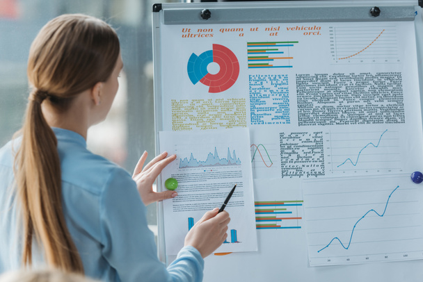 back view of young businesswoman pointing with pen at infographics on flipchart - Φωτογραφία, εικόνα