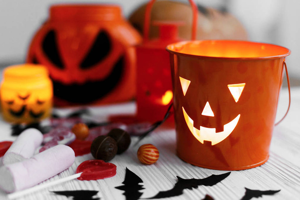 Halloween jack o lámpa vödör, izzó gyertya, ünnepi cukorka, koponyák, fekete denevérek, szellem, pók dekoráció fehér fa háttér. Térmásolat. csokit vagy csalunk - Fotó, kép
