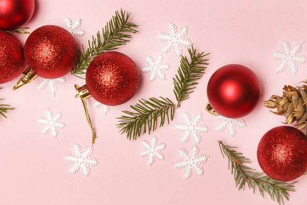 Red Christmas shiny balls and fir twigs on pale pink background. Christmas ornaments arrangement. - Foto, afbeelding