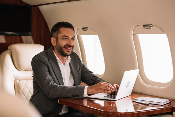 selective focus of happy bearded businessman using laptop in first class  - Foto, imagen
