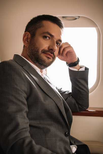 όμορφος επιχειρηματίας κάθεται κοντά στο παράθυρο του αεροπλάνου σε ιδιωτικό τζετ  - Φωτογραφία, εικόνα