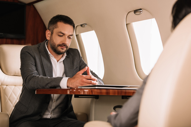 Selektiver Fokus eines gutaussehenden Geschäftsmannes, der neben Geschäftsfrau im Flugzeug sitzt  - Foto, Bild