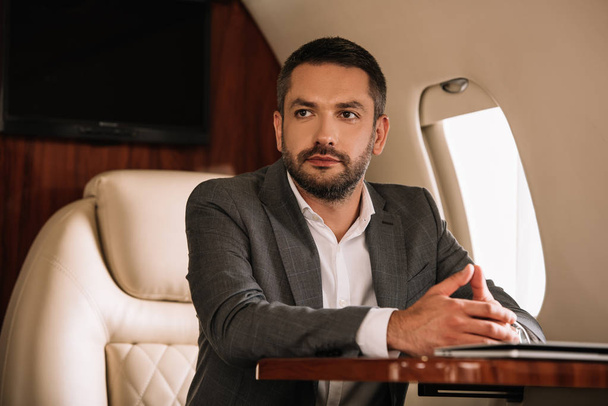 selective focus of handsome businessman sitting with clenched hands in private jet  - Fotografie, Obrázek