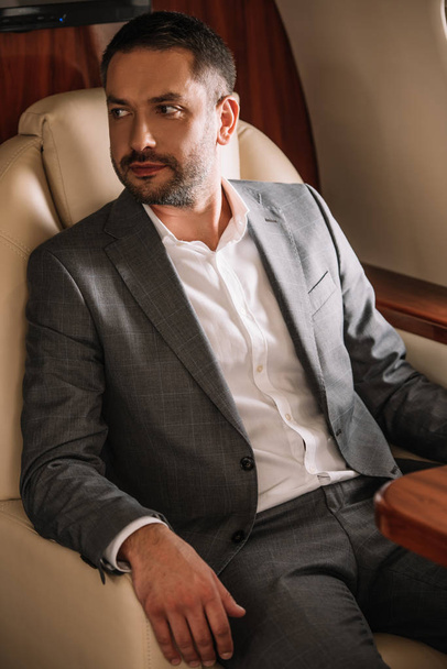 selective focus of bearded businessman in suit sitting in private jet  - Fotoğraf, Görsel