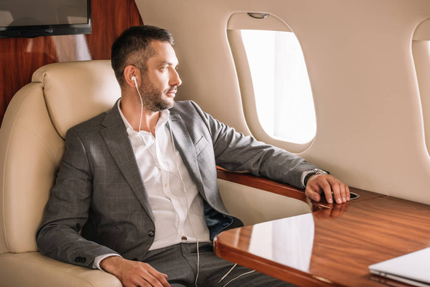 selective focus of handsome businessman listening music and looking at airplane window  - Foto, imagen
