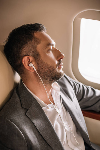 όμορφος επιχειρηματίας ακούει μουσική κοντά στο παράθυρο του αεροπλάνου  - Φωτογραφία, εικόνα