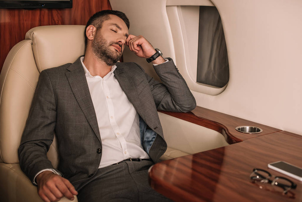 selectieve focus van zakenman met gesloten ogen zittend in prive jet  - Foto, afbeelding