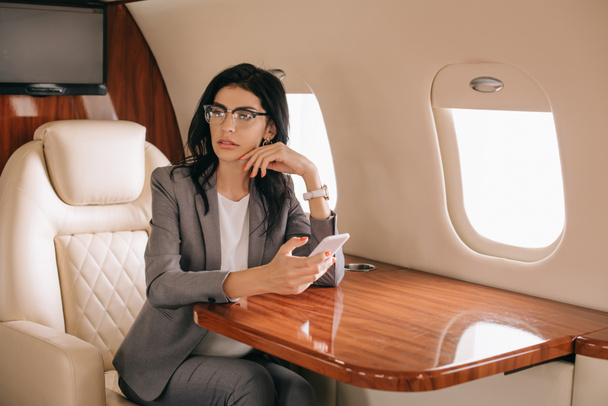 mujer de negocios en gafas usando smartphone en jet privado
  - Foto, Imagen