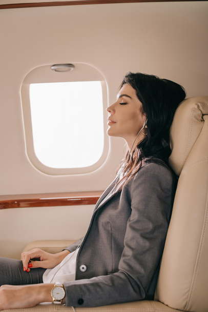 side view of attractive businesswoman listening music in private jet  - Foto, Bild