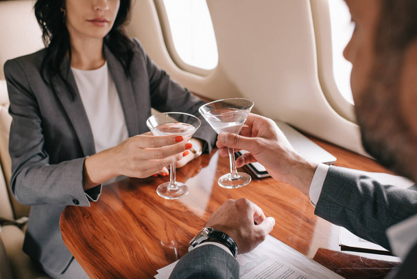 cropped view of bearded businessman and businesswoman toasting martini glasses in private jet  - Photo, Image