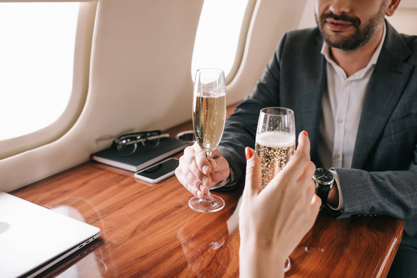 cropped view of woman and bearded man holding champagne glasses in private jet  - Foto, imagen