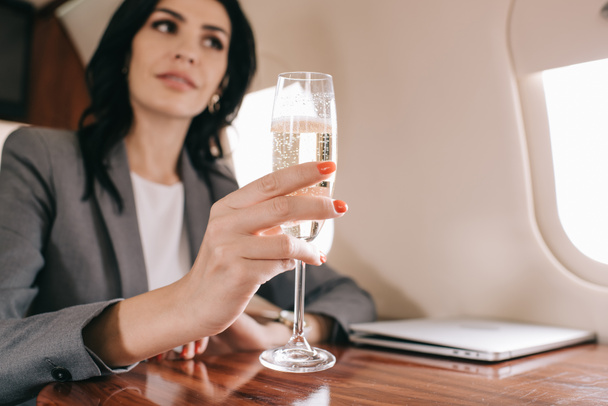 selective focus of champagne glass in hand of attractive businesswoman in plane  - Foto, Bild