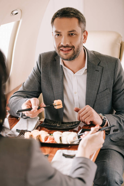 cropped view of businesswoman near bearded businessman and tasty sushi in private jet - 写真・画像