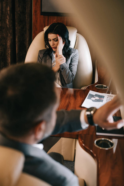 selective focus of scared businesswoman with fear of flight sitting with businessman in private jet  - Photo, Image