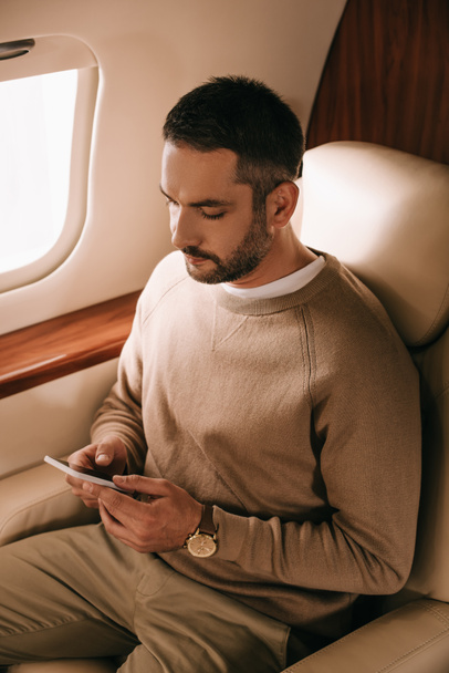 handsome bearded man holding smartphone in private jet  - Photo, Image