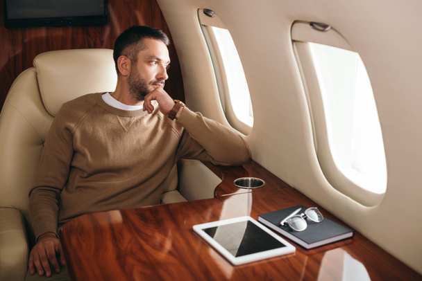 handsome bearded man looking at airplane window in first class of private jet  - Fotoğraf, Görsel