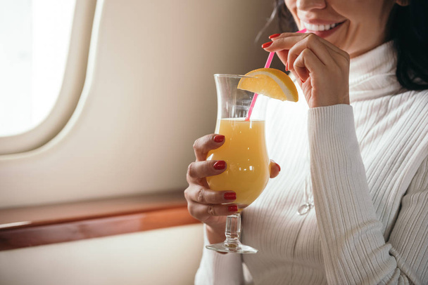 Ausgeschnittene Ansicht einer Frau mit leckerem Cocktail im Privatjet  - Foto, Bild