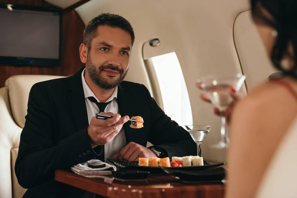 cropped view of woman holding martini glasses near handsome man in private jet  - Photo, Image