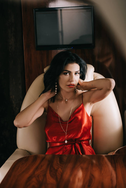 プライベートジェットに座っている赤いドレスの魅力的な女性の選択的な焦点  - 写真・画像