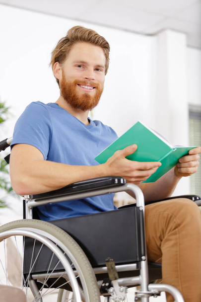 hymyilevä fyysisesti vammainen mies pyörätuolissa kirjojen ja kynän kanssa
 - Valokuva, kuva