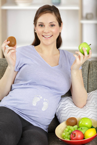 pregnant woman sitting on couch and holding fruits - Fotografie, Obrázek