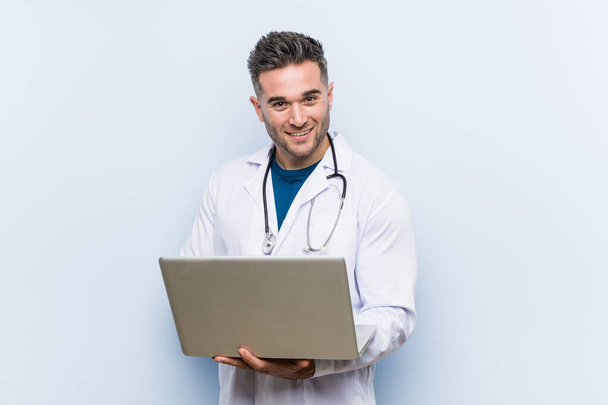 Caucásico médico hombre sosteniendo un ordenador portátil feliz, sonriente y alegre
. - Foto, Imagen