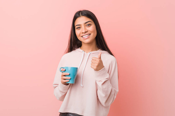 Young arab woman holding a cup smiling and raising thumb up - Foto, Imagem