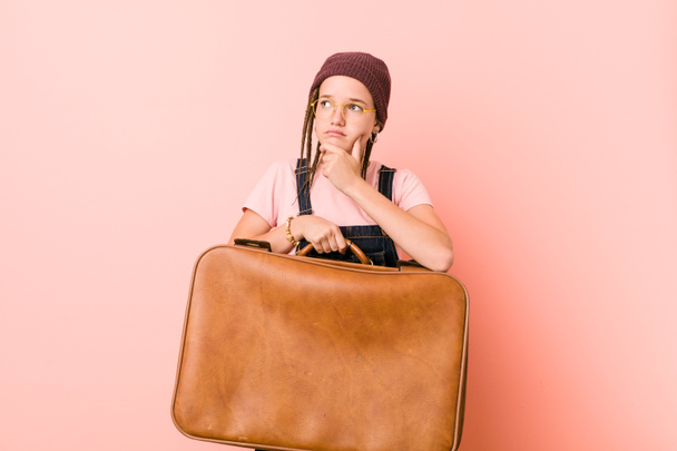 Молодая кавказка, держащая чемодан, смотрит в сторону с сомнительным и скептическим выражением лица
. - Фото, изображение