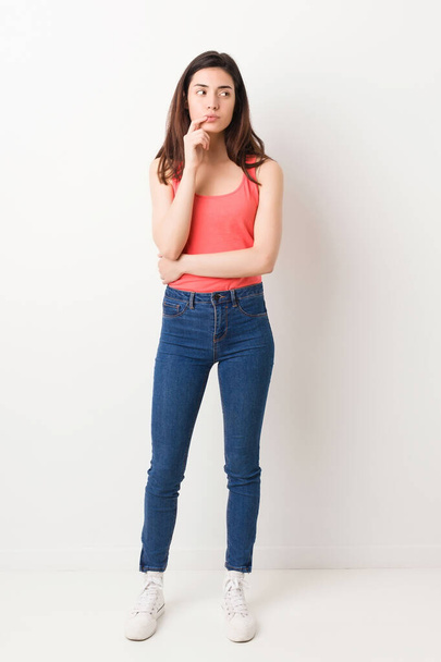 Full body young woman on white background looking sideways with doubtful and skeptical expression. - Photo, image