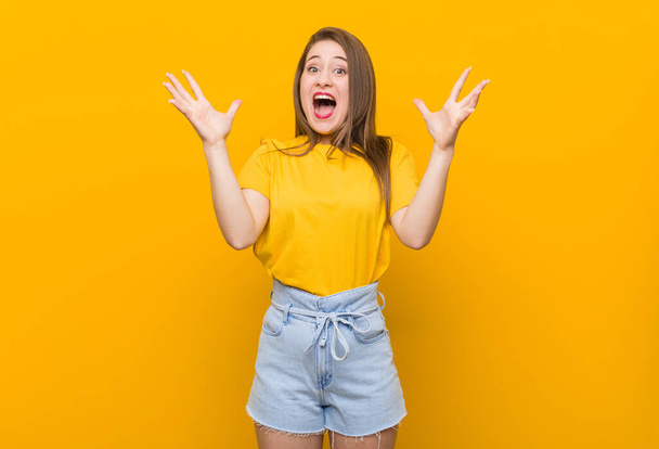 Młoda kobieta nastolatka w żółtej koszuli świętującej zwycięstwo lub sukces, jest zaskoczony i zszokowany. - Zdjęcie, obraz