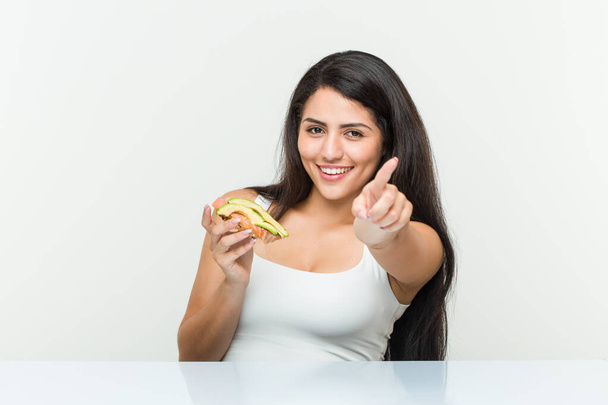 Avokado tostu tutan genç İspanyol kadın öne doğru gülümsüyor.. - Fotoğraf, Görsel