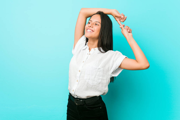 Νεαρή ισπανόφωνη γυναίκα σε μπλε τοίχο απλώνει τα χέρια, χαλαρή θέση. - Φωτογραφία, εικόνα