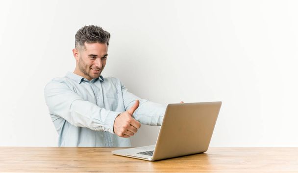 親指でノートパソコンを操作する若いハンサムな男は、何かについての歓声、サポートと尊敬の概念. - 写真・画像