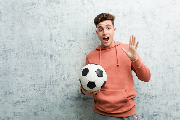 Młody sportowiec trzyma piłkę nożną świętując zwycięstwo lub sukces - Zdjęcie, obraz