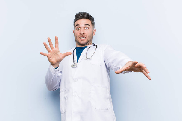 Young handsome doctor man being shocked due to an imminent danger - Foto, Imagen
