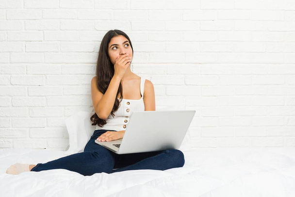 Nuori arabi nainen työskentelee hänen laptop sängyllä huomaavainen etsivät kopio tilaa kattaa suun käsin
. - Valokuva, kuva