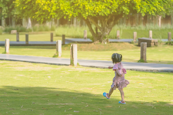 ein kleines Mädchen im rosafarbenen Rock genießt eine entspannte Zeit beim Spielen auf dem grünen Rasen im öffentlichen Park am Abend. - Foto, Bild
