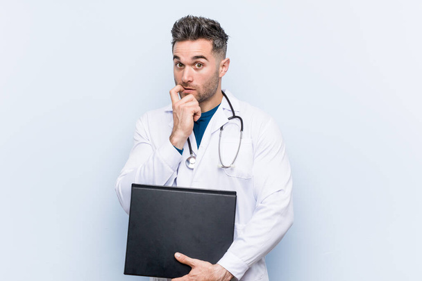 Καυκάσιος γιατρός κρατάει ένα φάκελο χαλαρό σκεπτόμενος κάτι κοιτάζοντας ένα χώρο αντιγραφής. - Φωτογραφία, εικόνα