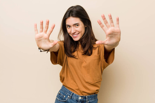 jonge brunette vrouw tegen een beige achtergrond tonen nummer tien met handen. - Foto, afbeelding