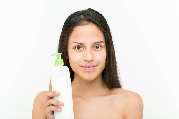 Close up of a beautiful and natural hispanic young woman holding a moisturizing cream bottle - Photo, Image